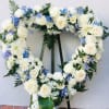 Heart-shaped floral wreath with white roses and blue flowers on an easel
