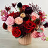 Mixed bouquet of red, pink, and burgundy flowers in a blush vase