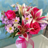 Pink roses and lilies in a white vase with a pink ribbon