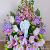 Pink and purple floral arrangement with lilies and roses around a white angel figurine