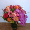 Colorful bouquet of roses, dahlias, calla lilies, and orchids in a glass vase