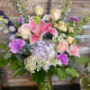 Mixed pastel bouquet with lilies, roses, hydrangea, and purple accents in a glass vase