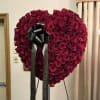 Heart-shaped arrangement of red roses with a black ribbon bow