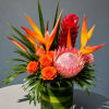 Tropical arrangement with orange roses and a pink protea in a green vase