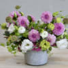 Low arrangement of pink dahlias with white and green blooms in a gray pot.