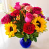 Mixed bouquet of roses, sunflowers, and carnations in a blue glass vase