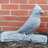 Gray bird statue perched on a faux log against a brick wall