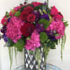 Tall arrangement of hot pink hydrangeas, red roses, and purple blooms in a silver patterned vase