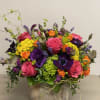 Vibrant arrangement of pink roses, purple blooms, orange flowers and green accents in a rustic ceramic container.