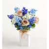 Bouquet of peach roses, blue flowers, and white blooms in a white vase