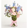 Mixed bouquet of blue, white, and pink flowers in a glass vase with a pink ribbon