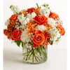 Orange roses and white flowers arranged in a clear glass vase