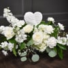 White floral arrangement with roses and carnations around a heart ornament