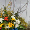 Large mixed floral arrangement with white, yellow, and orange blooms and a blue ribbon