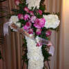 White floral cross with pink roses and ribbon on an easel
