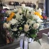Large white and yellow flower arrangement in a glass vase with a white ribbon