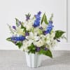 White lilies, roses, and blue delphinium in a white vase