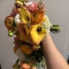 Handheld bouquet with yellow calla lilies, orange ranunculus, and pink blooms
