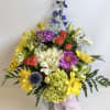 Mixed bouquet of yellow daisies, roses, and purple flowers in a glass vase