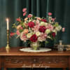 Pink and red floral arrangement in a metal vase beside a lit candle