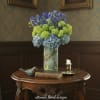 Blue and green hydrangea arrangement in a painted vase on a wooden table