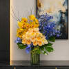 Yellow and peach roses with blue flowers in a glass vase