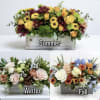 Three seasonal floral arrangements in wooden boxes labeled summer, winter, and fall.