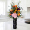 Tall bouquet of orange and pink flowers in a black vase