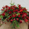 Large red rose arrangement with mixed greenery on a burlap-draped stand