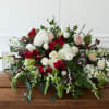 This abundant casket spray features velvet red roses and seasonal blooms in