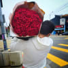 Large armful bouquet of tightly packed red roses wrapped in kraft paper, carried on a person's shoulder