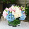 Pink and white bouquet with blue hydrangeas in a square glass vase