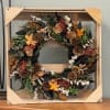 Rustic wreath with pinecones, dried orange slices, and orange flowers in a wooden frame