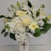 Tall white and cream flower arrangement with lilies, roses, hydrangeas and gerberas in a white vase with a silver cross.
