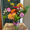 Mixed bouquet of orange, pink, and yellow flowers in a glass vase with a ribbon