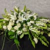 White floral casket spray with lilies, roses, and trailing greenery