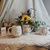 Flower arrangement in a mug surrounded by decorative quote mugs