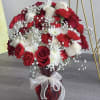 Red and white rose bouquet in a red glass vase with a white ribbon