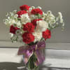 Bouquet of red carnations and white roses in a glass vase with a purple ribbon