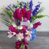 Tall bouquet of pink, blue, purple, and white flowers in a glass vase