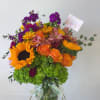 Bouquet of sunflowers, orange roses, and purple blooms in a glass vase