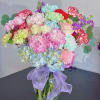 Colorful bouquet of carnations, roses, and hydrangeas in a glass vase with a purple ribbon