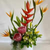 Tropical flower arrangement with red and orange blooms in a white vase