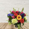 Mixed bouquet of roses, gerbera daisy, hydrangea, and blue blooms in a glass vase