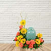 Coral roses and yellow sunflowers arranged around a teal urn.