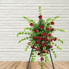Standing floral spray of red roses with trailing green foliage on an easel
