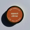 Round candle tin labeled "sunset citrus" on a plain surface