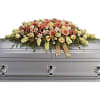 Large floral spray on a silver casket with peach and cream flowers