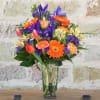 Mixed bouquet of orange, purple, pink, and yellow flowers in a clear glass vase