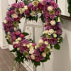 Heart-shaped floral wreath of pink, purple, and white roses on a stand